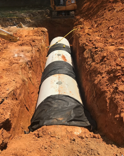 A large pipe is laying in the dirt in a trench.