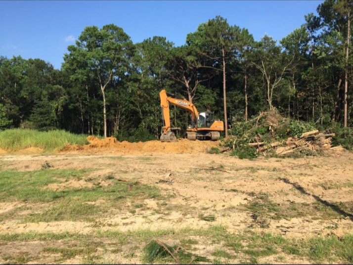 An excavator is moving dirt in a field with trees in the background.