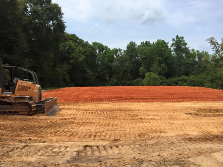 A bulldozer is moving dirt in a field with trees in the background.