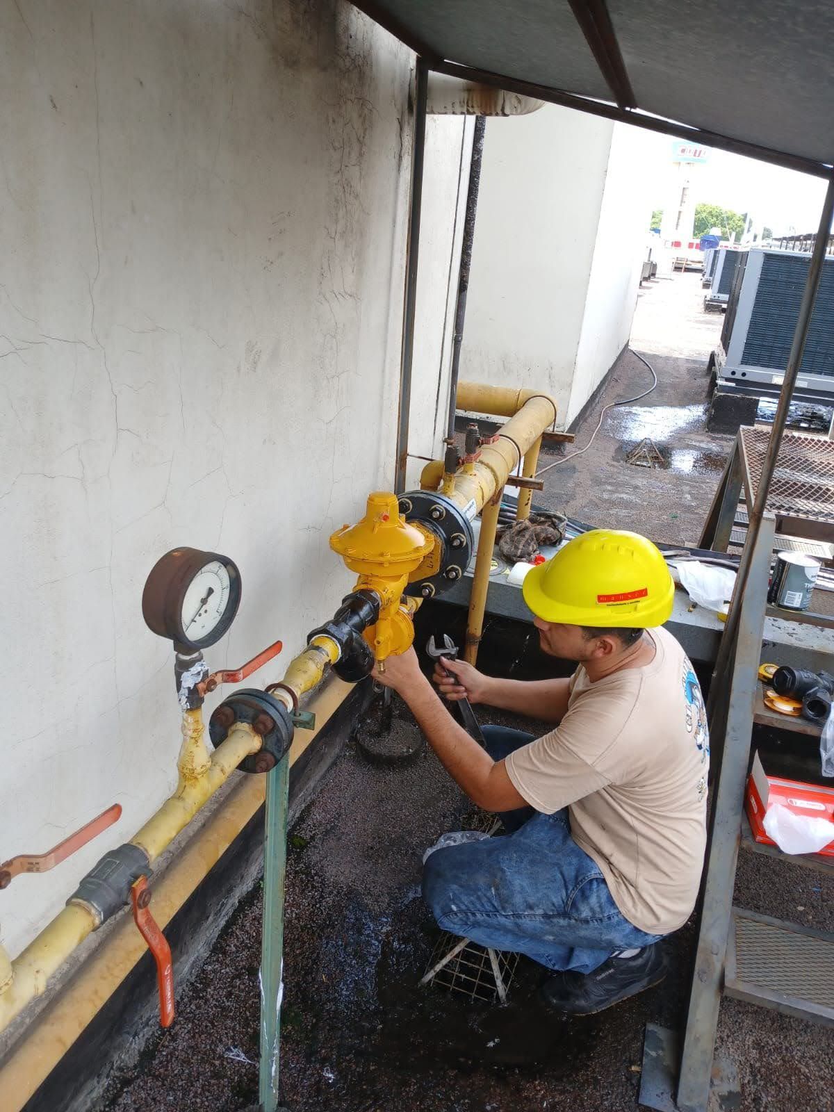 Dos trabajadores con overoles azules y cascos inspeccionan maquinaria con tuberías en un entorno industrial.