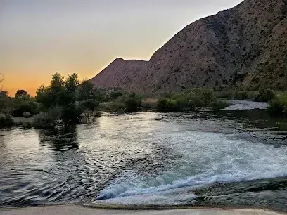 Tree Removal Service West Covina Calm river flows past rocky hills at sunset with scattered trees.