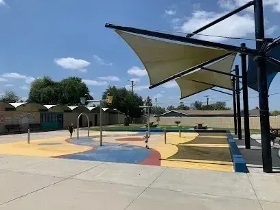 Tree Removal Service West Covina -A colorful outdoor splash pad with geometric shade sails and a few children playing on a sunny day.