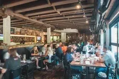 Tree Services West Covina Patrons enjoy food and drinks at tables within a busy, rustic restaurant with a long bar.