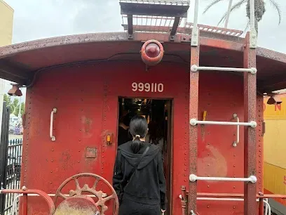 Tree Services West Covina-A person in a black hoodie enters a vintage red train car numbered 999110. The scene conveys curiosity and adventure, set against a cloudy sky.