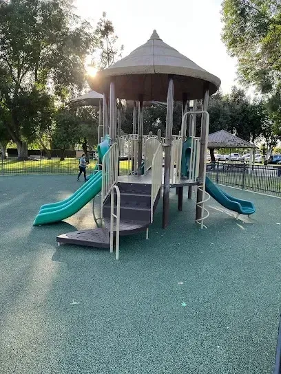 Tree Removal Service West Covina featuring a modern playground structure with slides, climbing areas, and safety flooring, surrounded by trees and fencing in a park setting