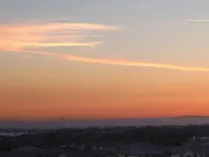 Tree Removal Service West Covina -A hazy sunset sky with orange and pink hues above a silhouetted cityscape and distant mountains.