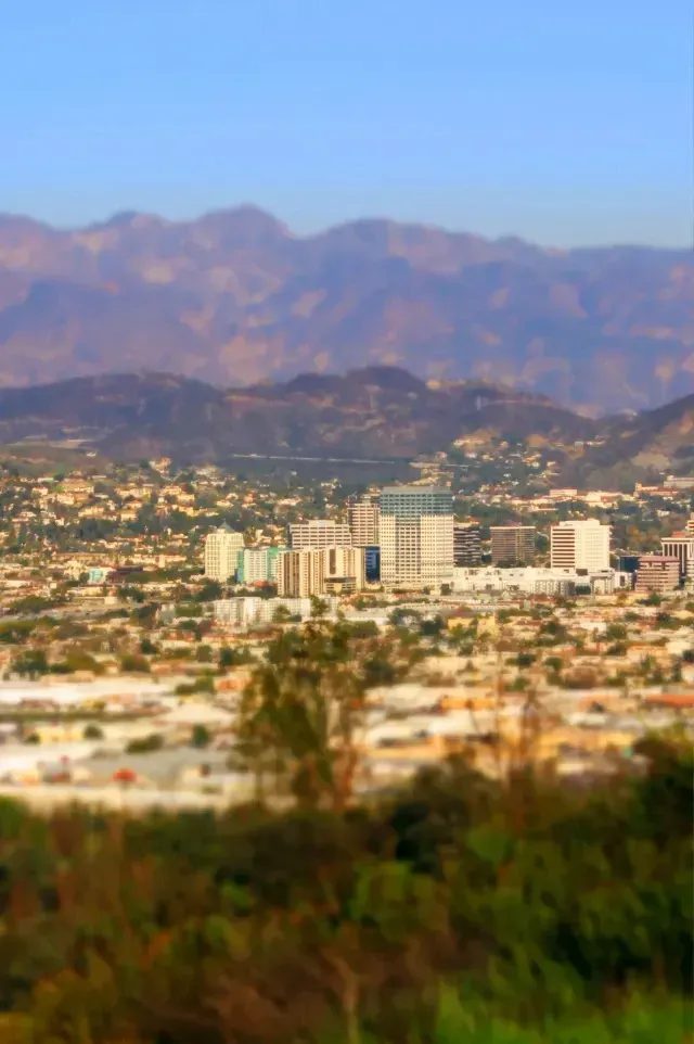 Tree Removal Service West Covina – This image shows a scenic view of Azusa, California, with modern high-rise buildings in the center surrounded by suburban neighborhoods. In the background, mountain ranges rise under a clear blue sky, adding a natural backdrop to the urban landscape