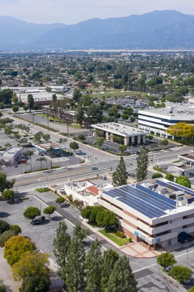 Tree Removal Service West Covina shows an aerial view of a suburban area with commercial buildings, tree-lined streets, and mountains in the background under a clear sky.