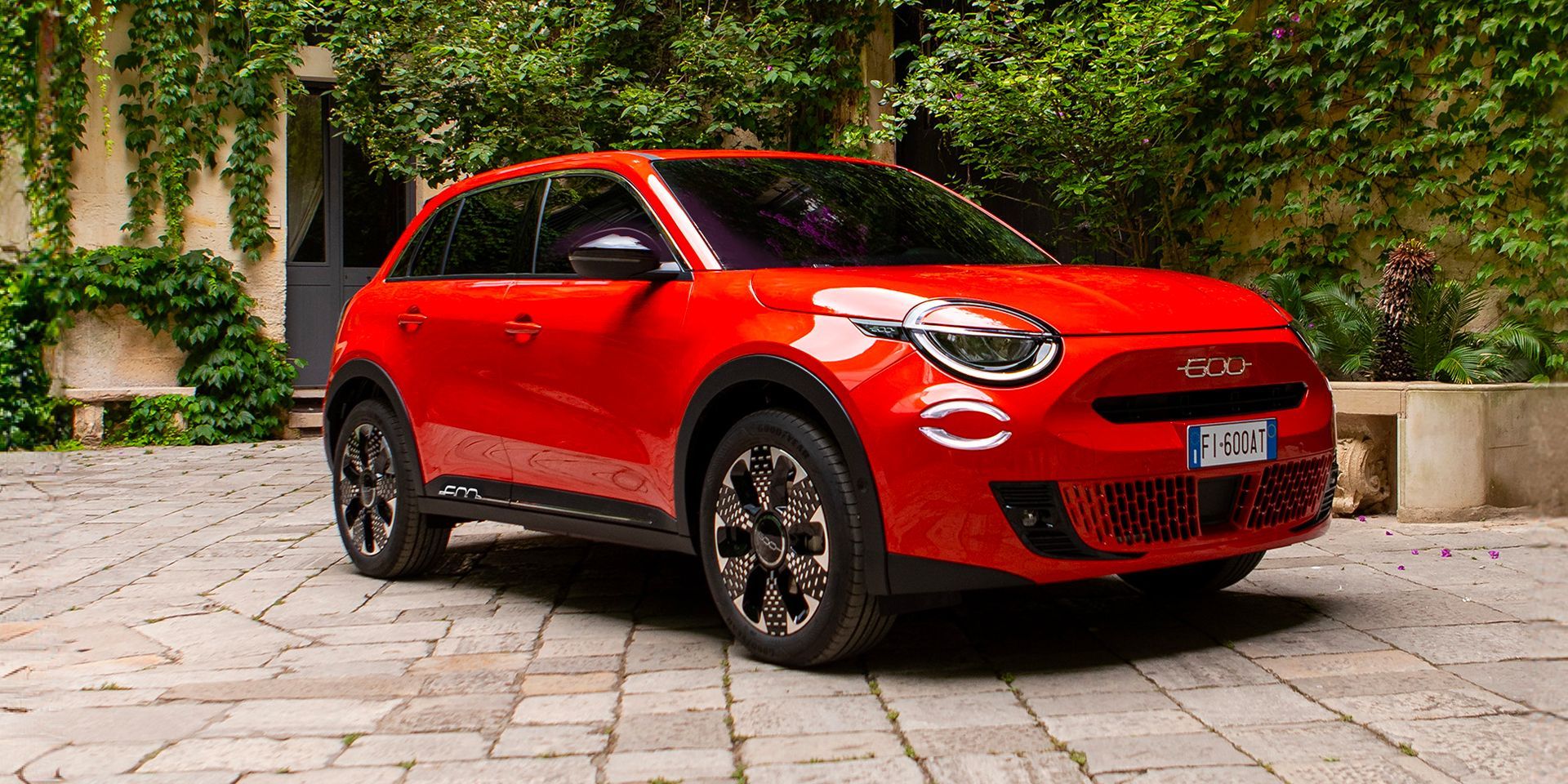 Une voiture rouge est garée sur une allée en briques devant un bâtiment.