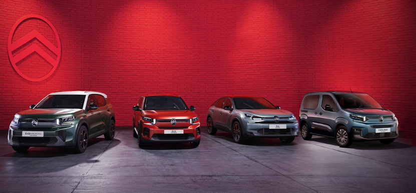 Une rangée de voitures Citroën est garée devant un mur rouge.