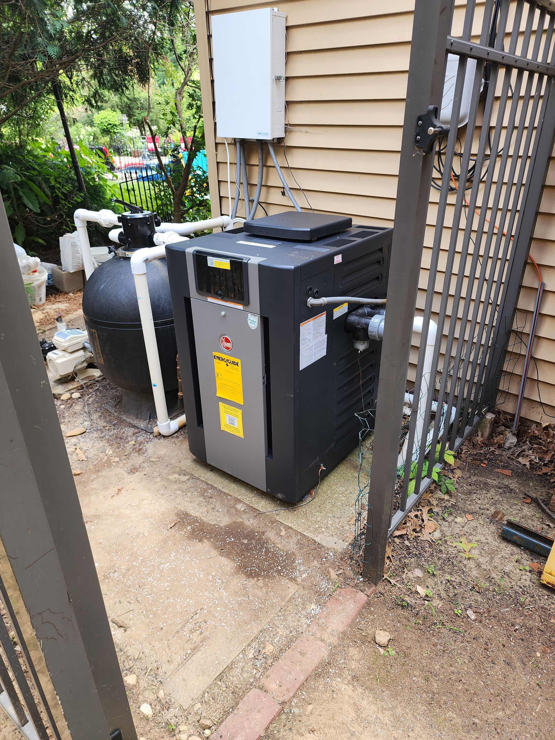A pool heater is sitting outside of a house next to a fence.
