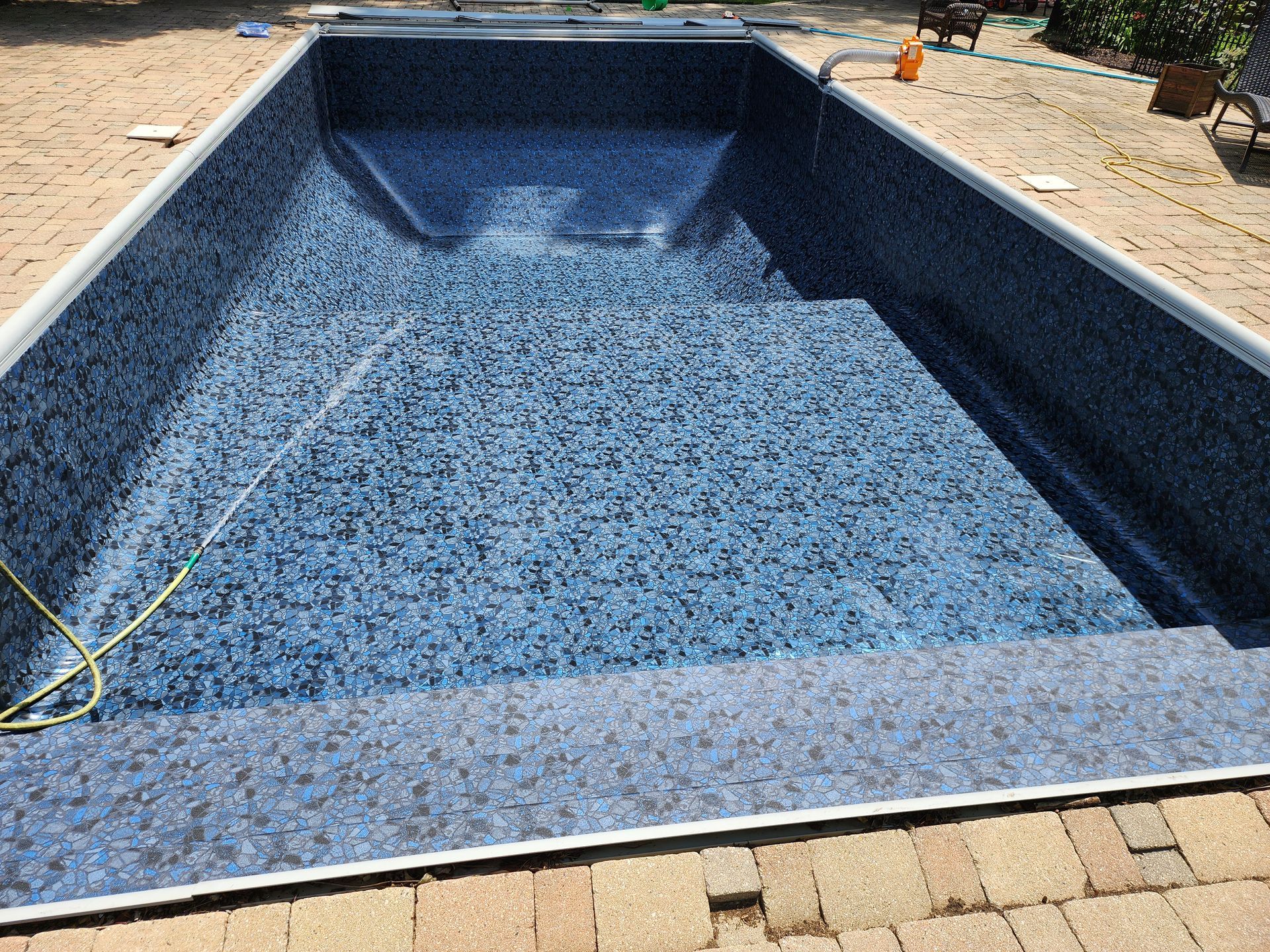 A large swimming pool is sitting on top of a brick patio.