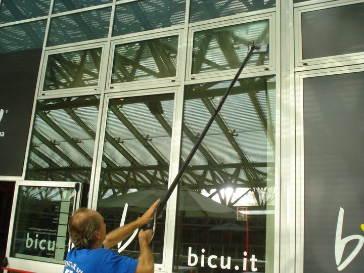 Un uomo con una camicia blu sta pulendo le finestre di un edificio su cui c'è scritto bicu.it