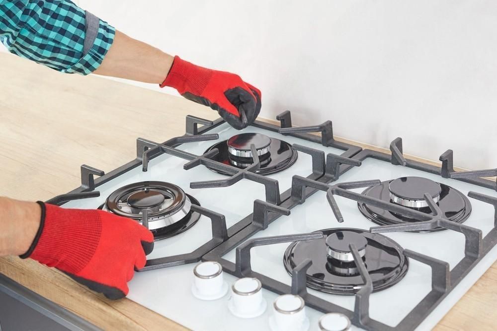 A person is fixing a gas stove in a kitchen.