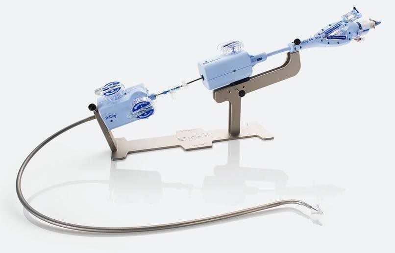 Dispositivo médico para procedimentos cardíacos, composto por componentes azuis e prateados montados em um suporte de metal. Um longo tubo flexível se estende do dispositivo.