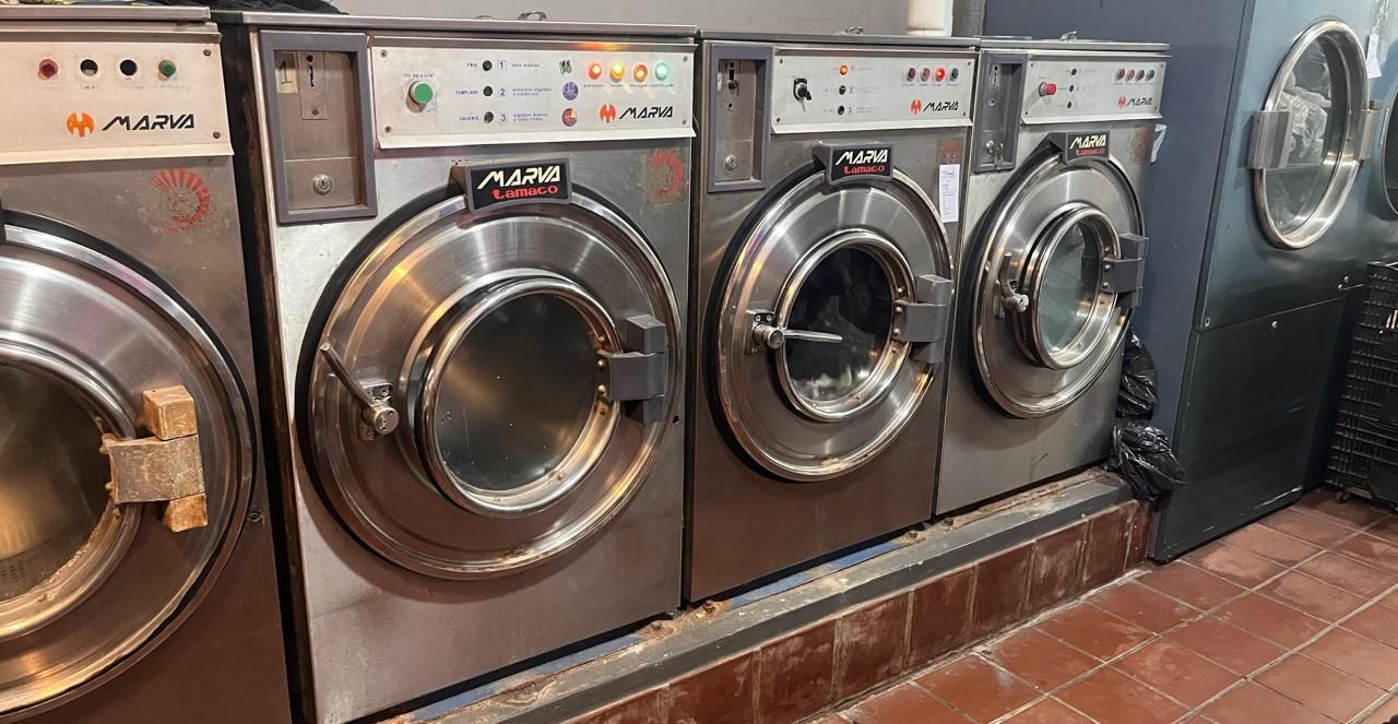 Una fila de lavadoras industriales que funcionan con monedas en una lavandería con suelos de baldosas.