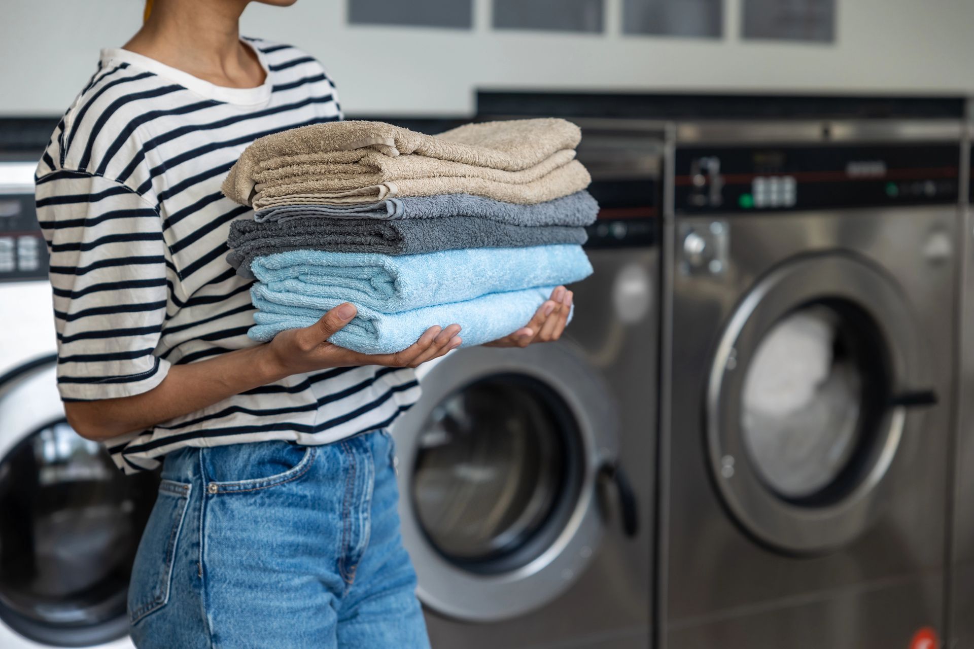 Una persona con una camisa a rayas y pantalones vaqueros sostiene una pila de toallas dobladas