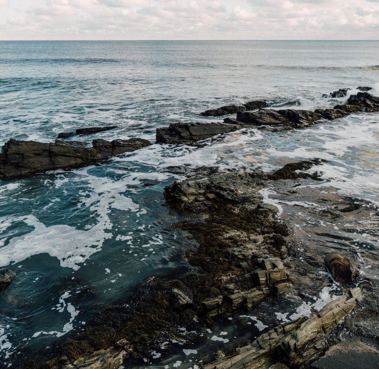 A rocky shoreline of the ocean with waves crashing against the rocks