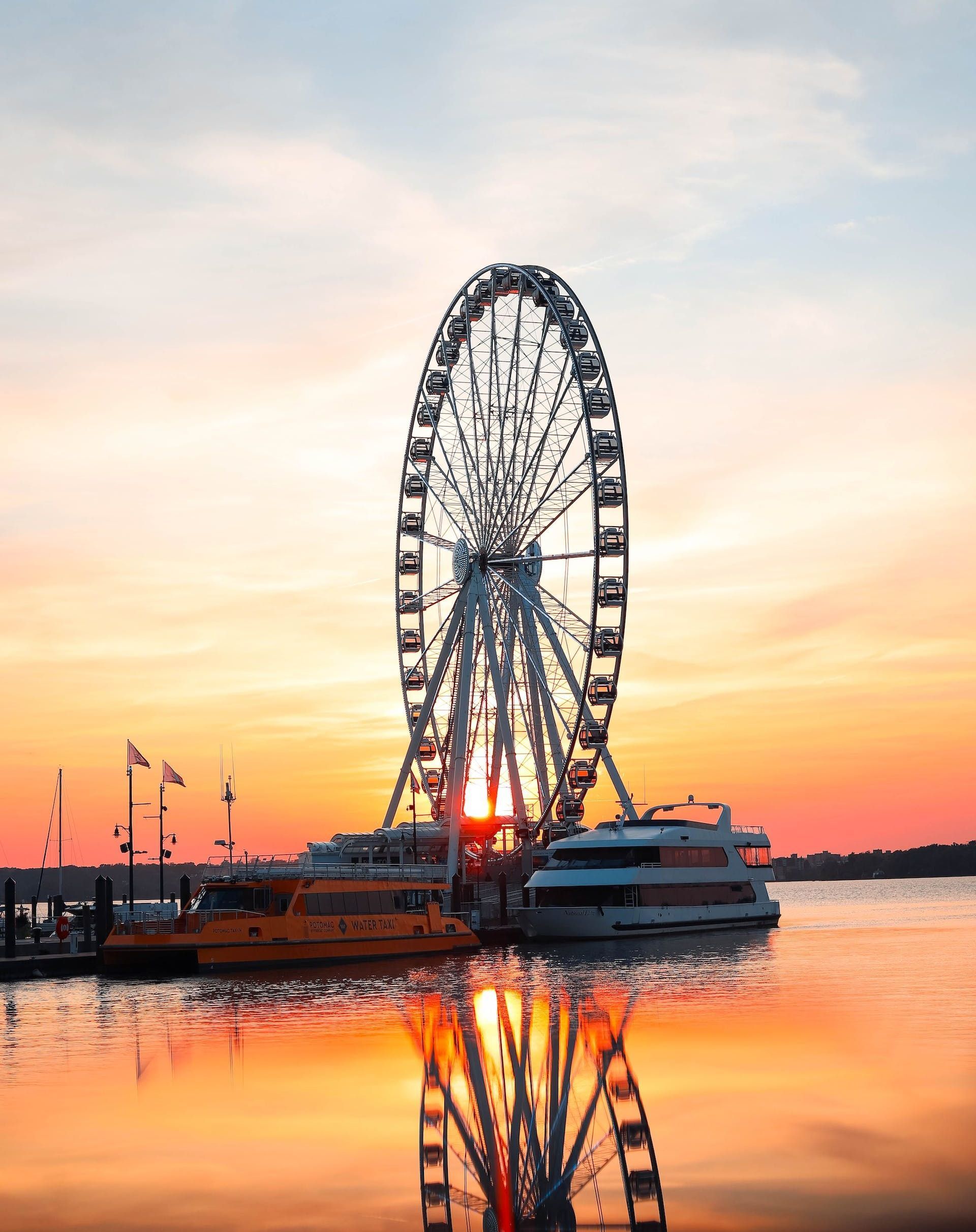 A ferris wheel is reflected in the water at sunset.