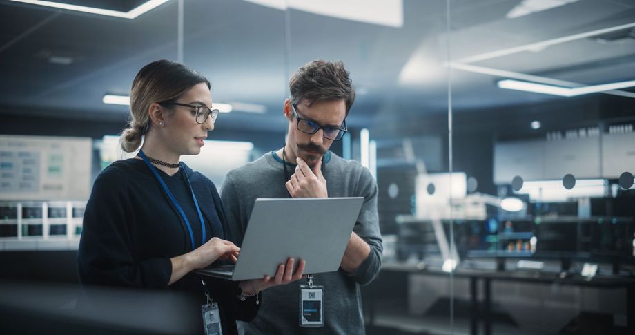 Two tech professionals in glasses looking at a laptop in a modern office.