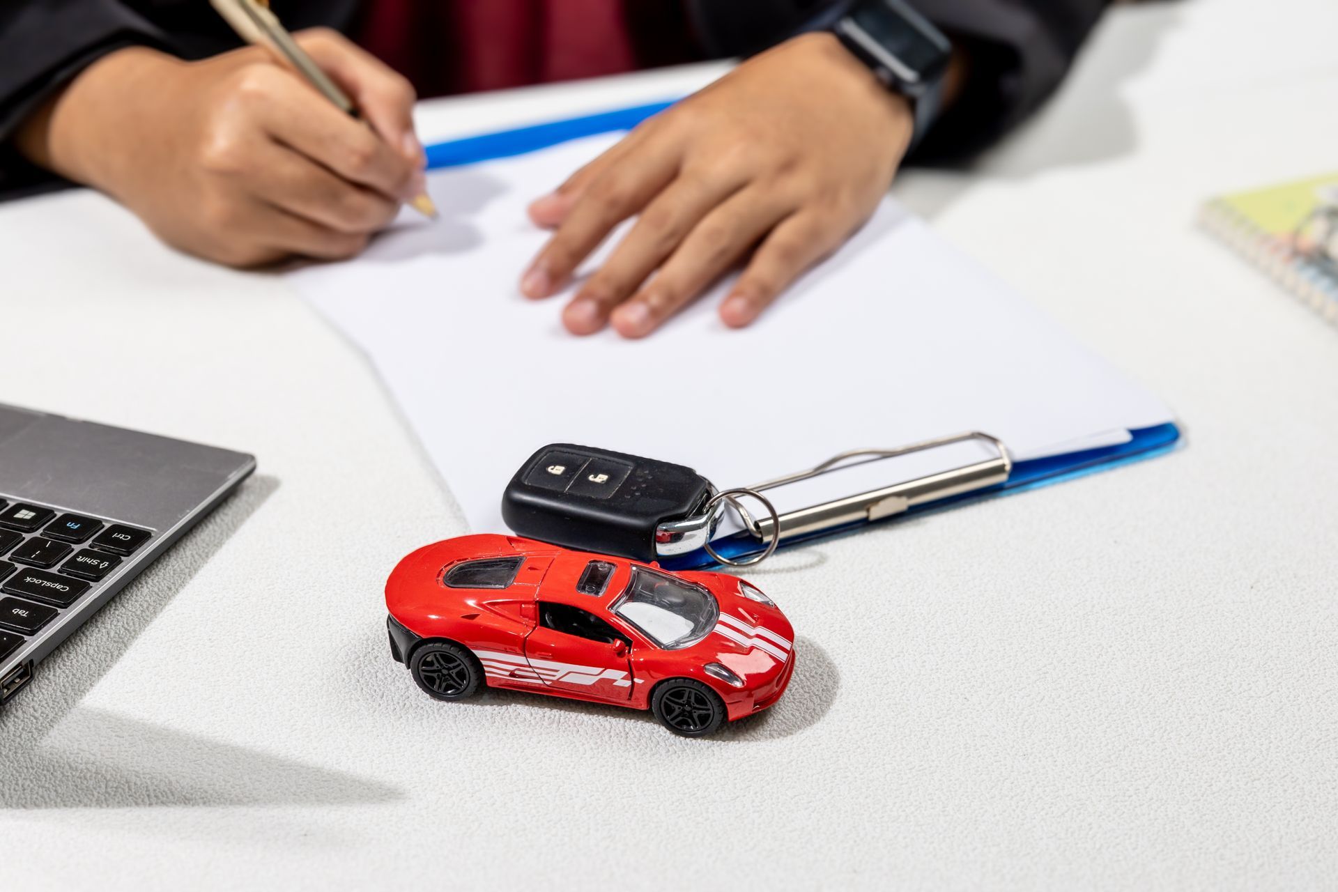 Person signing paperwork with car keys and a toy car on a table.