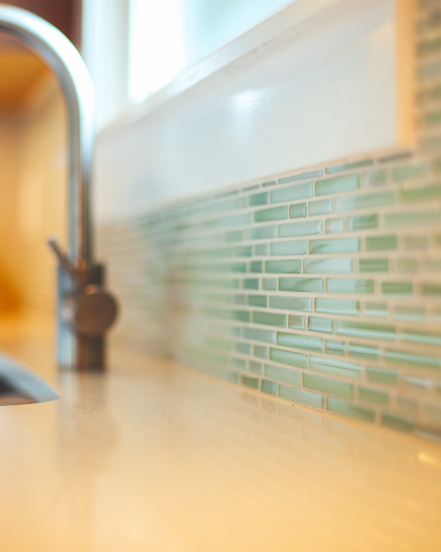 Kitchen sink with a chrome faucet and blue-green mosaic tile backsplash in soft daylight