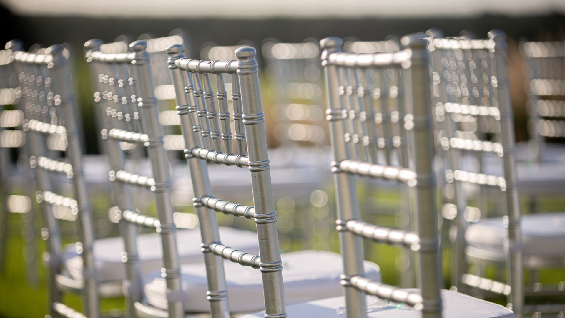A row of silver chiavari chairs are lined up in a row.