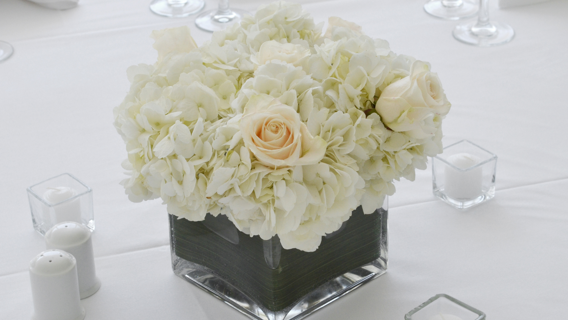 A vase filled with white flowers and candles on a table.