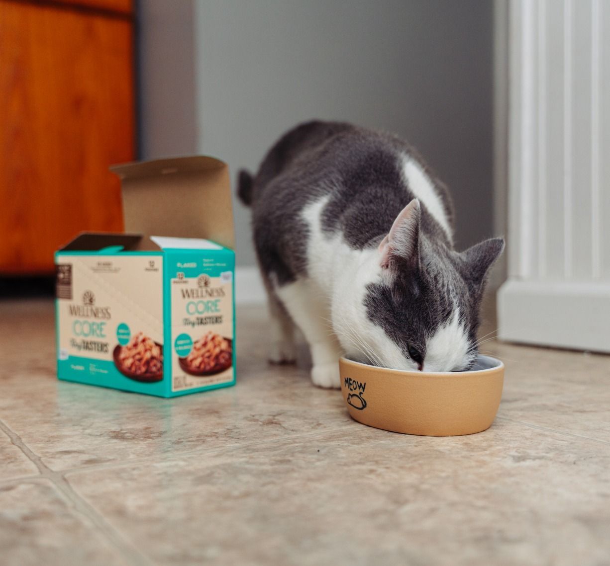 A cat is eating from a bowl next to a box of cat food
