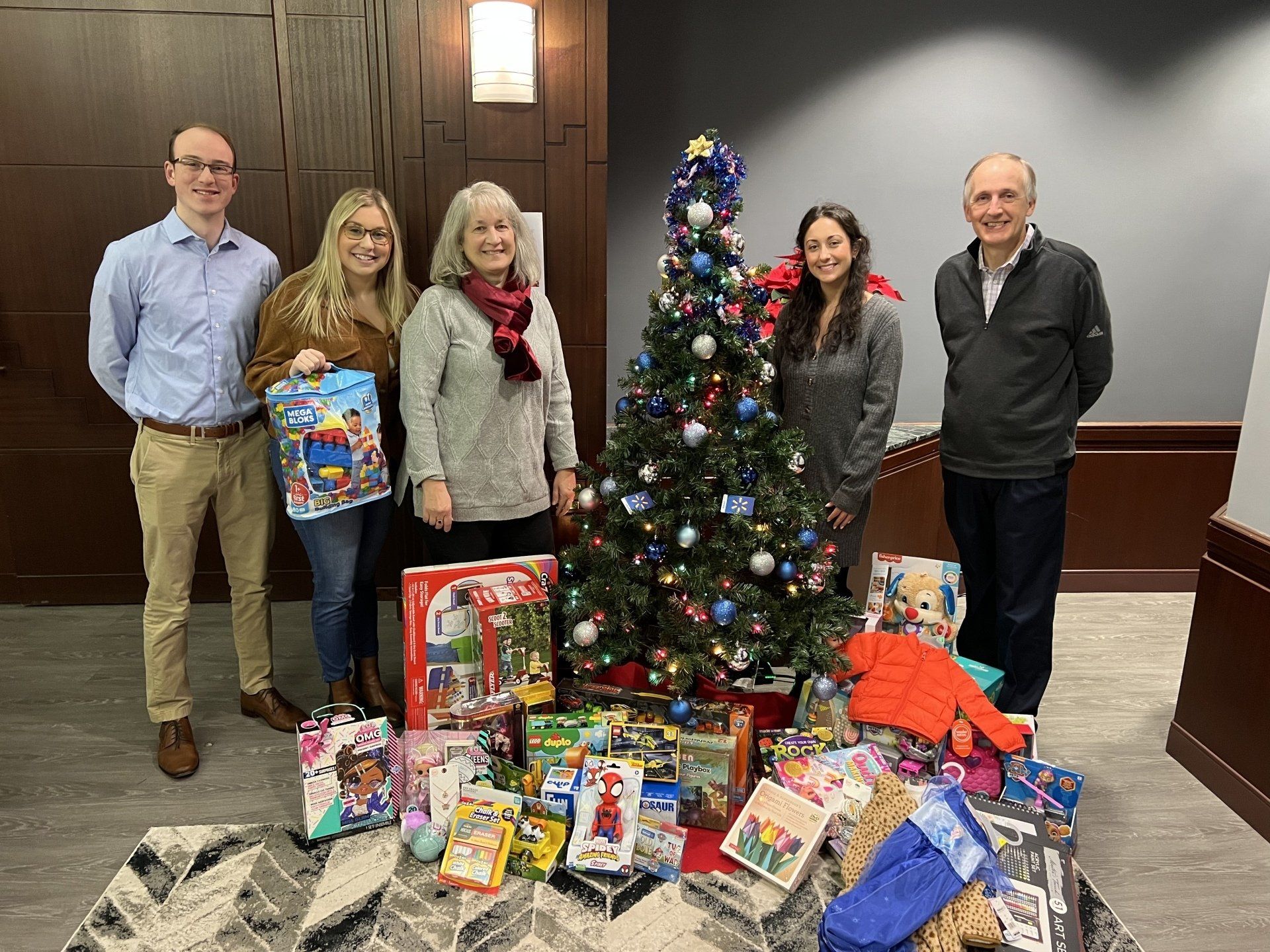 Eric, Lauren, Susan, Olivia, and Howard stand in front of MBK's lobby Christmas tree surrounded by the toys collected for the gift drive.