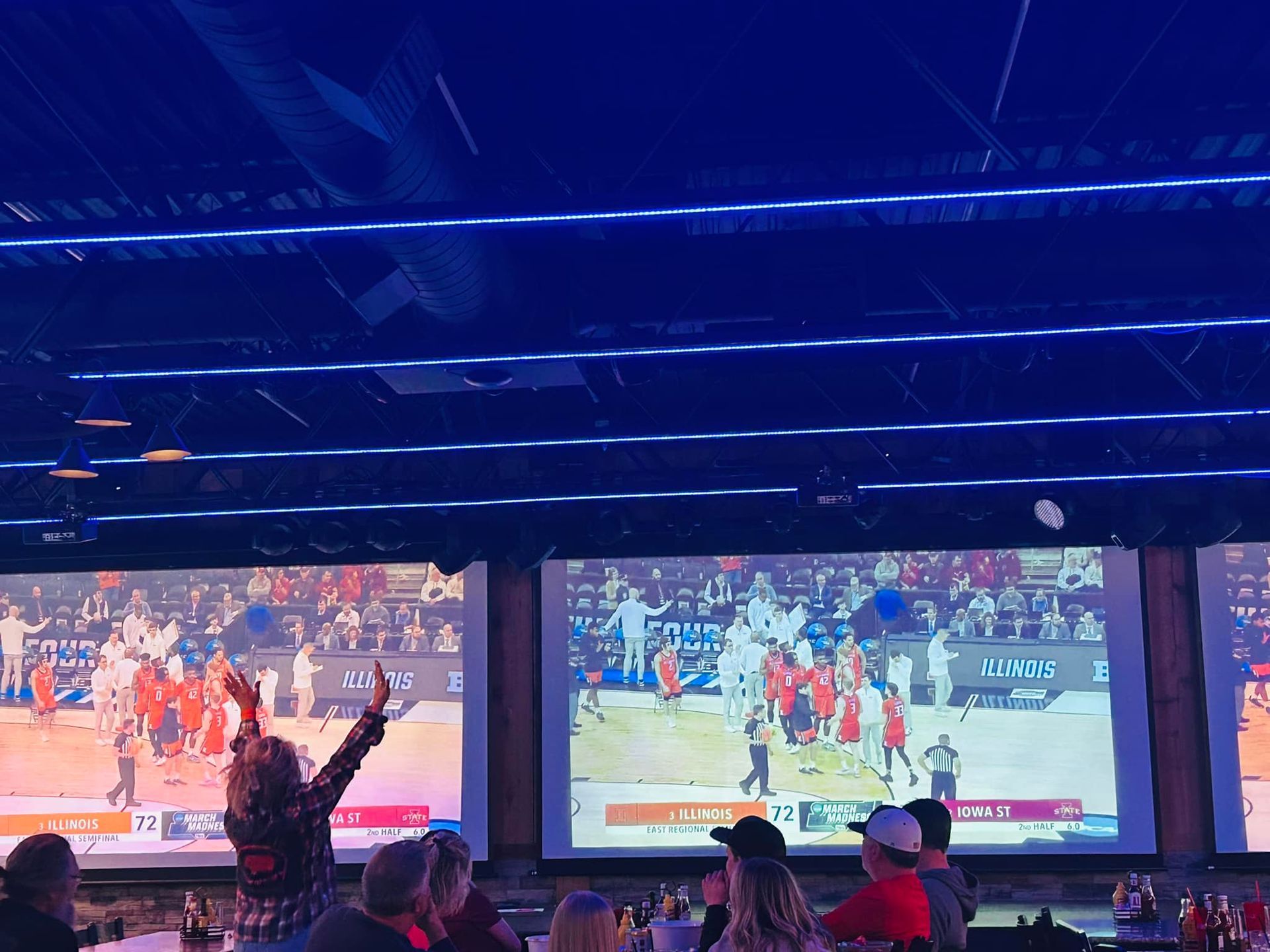 A group of people are watching a basketball game on a large screen.