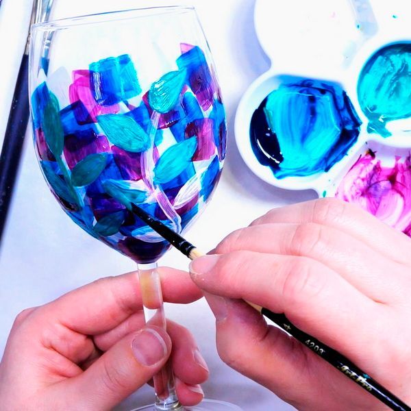 Una persona está pintando una copa de vino con pintura azul y morada.