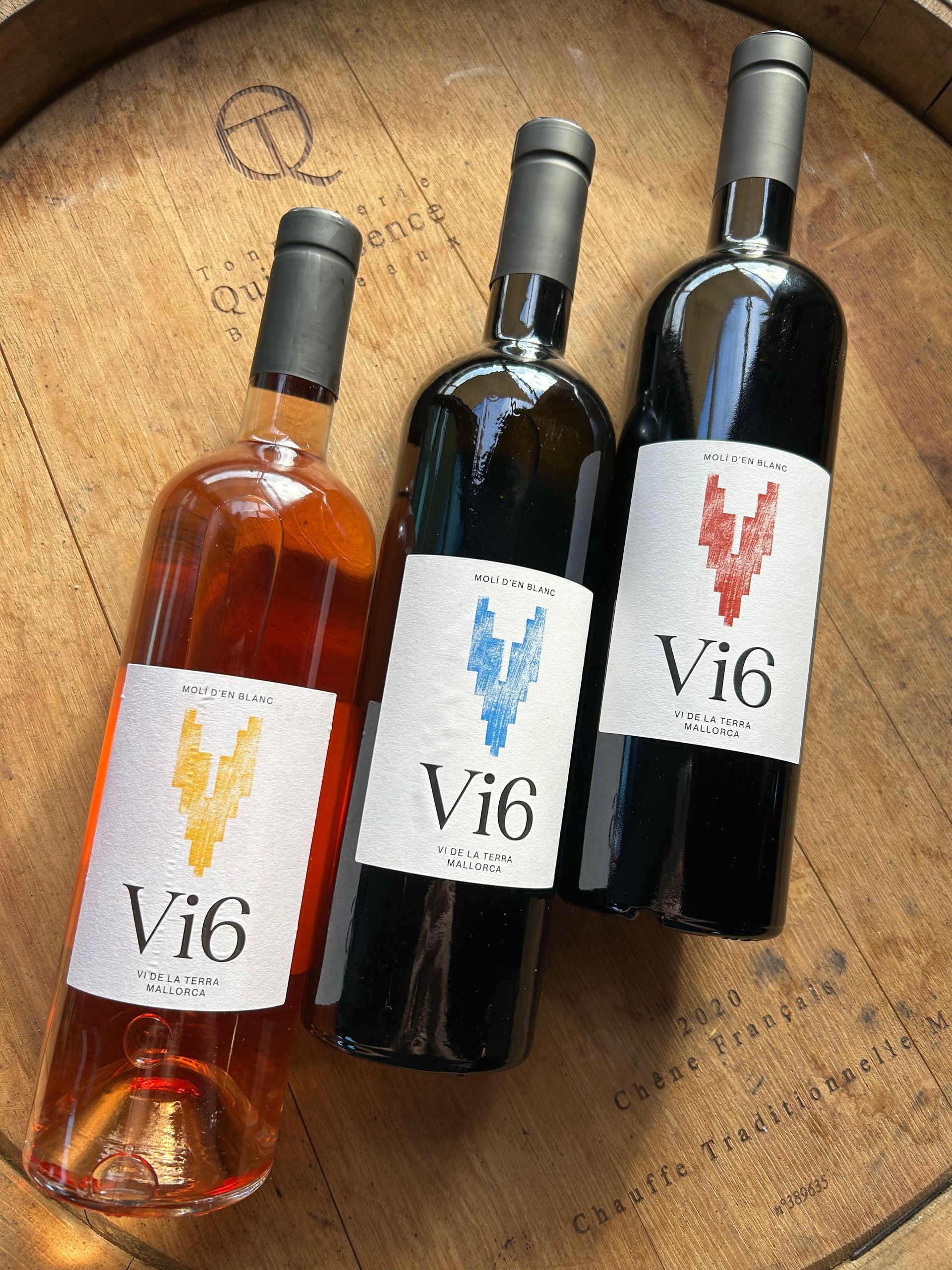 Tres botellas de vino vi6 están sobre un barril de madera