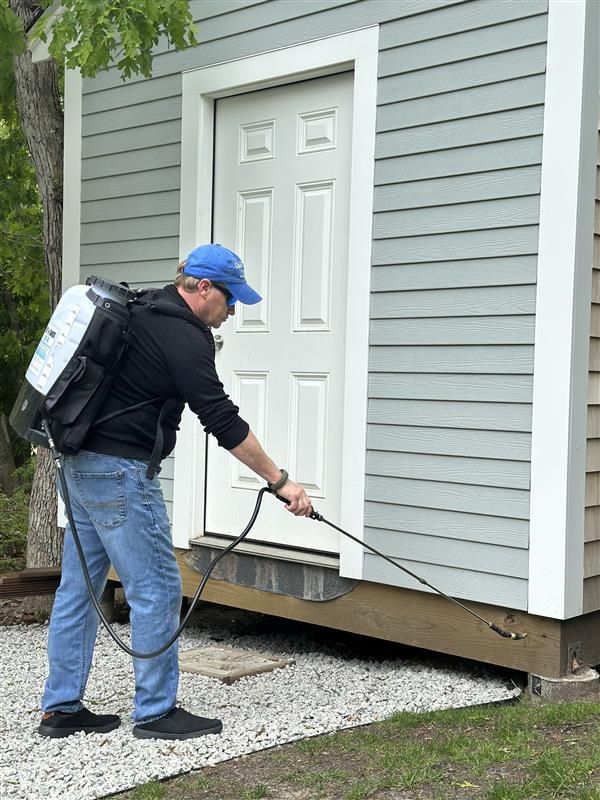 A man is spraying a house with a backpack sprayer.