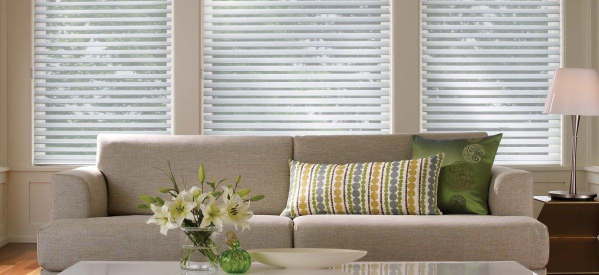 a living room with alta blinds, a couch and a table with a vase of flowers on it Love is Blinds Missouri (314) 808-3440.