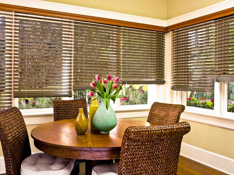 a dining room with wood and woven wood shades a table and chairs and a vase of flowers on the table Love is Blinds Missouri (314) 808-3440.
