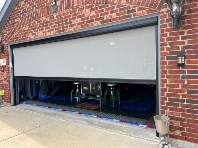 A red brick house has an exterior patio shade for the garage area. 