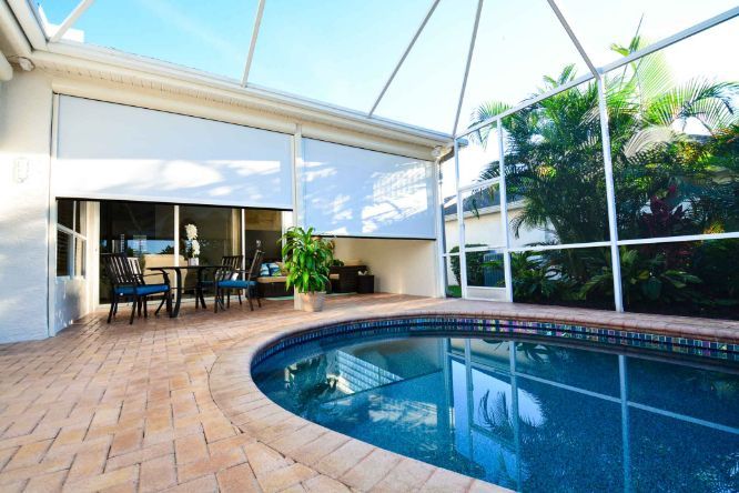 An outdoor patio with a pool has outdoor patio shades. 