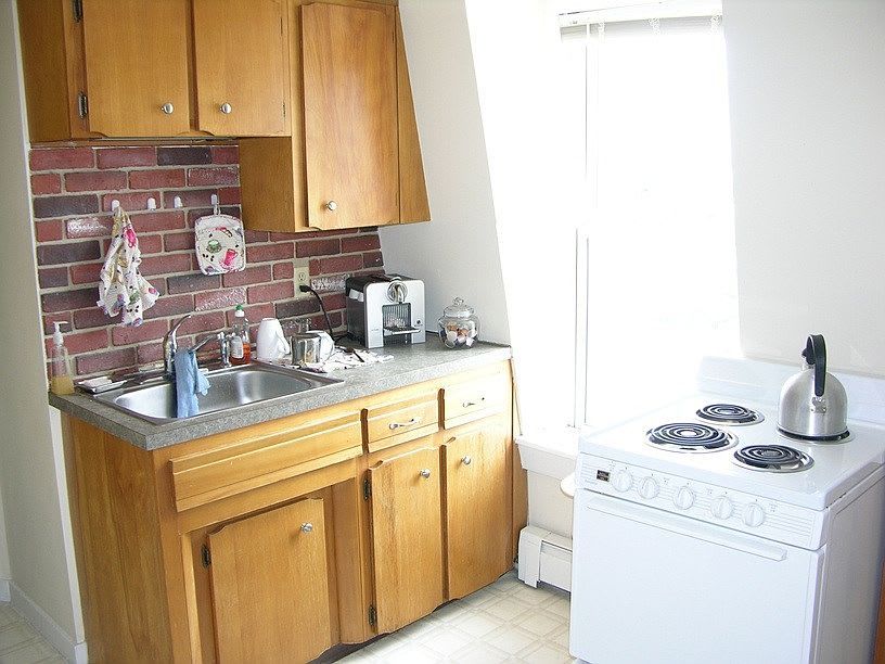 Small kitchen with wooden cabinets, brick backsplash, and a white stove.