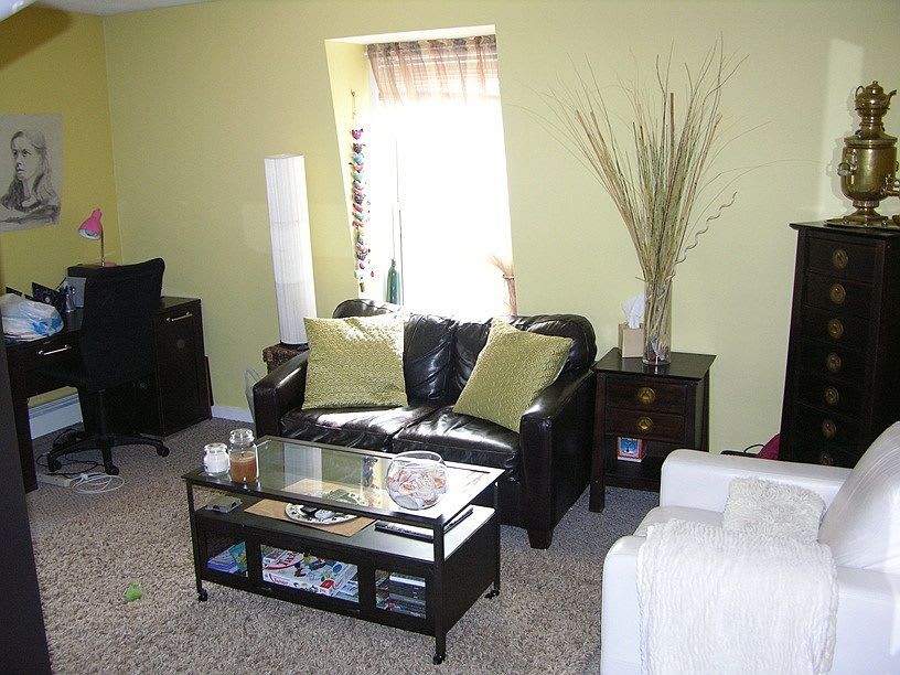 Living room with black leather sofa, white chair, black desk, and yellow walls.