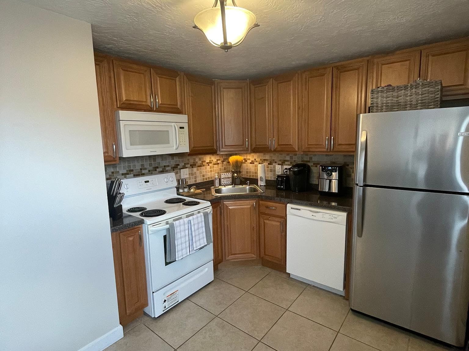 Small kitchen with wood cabinets, white appliances, and stainless steel refrigerator.