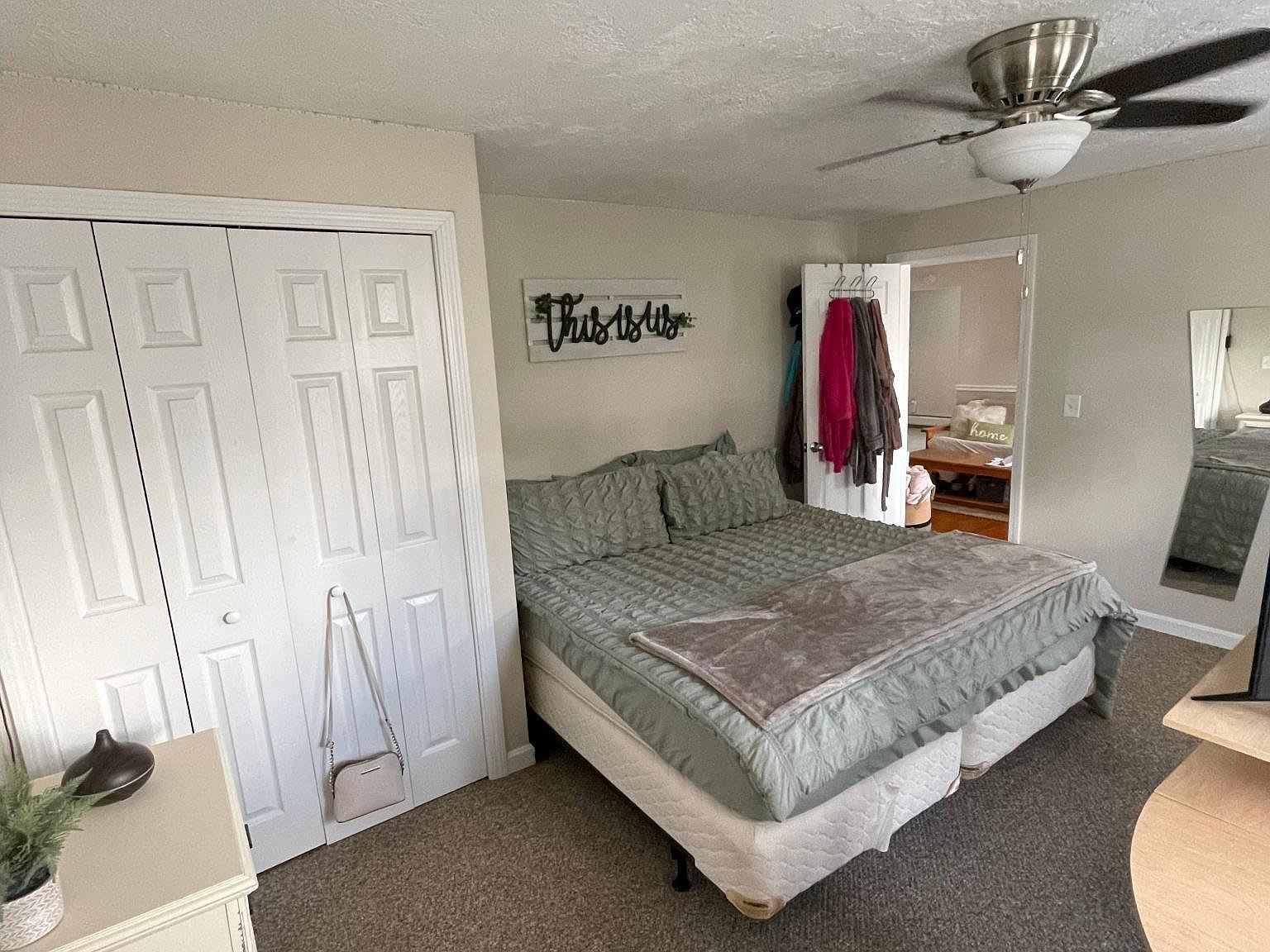 Bedroom with bed, closet, dresser, and ceiling fan. Light-colored walls and carpet.