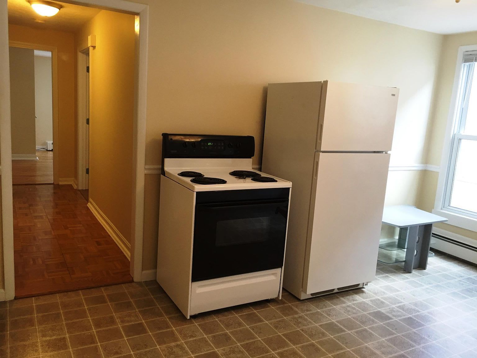 Kitchen with white appliances, including a stove and refrigerator, with a doorway leading to a hallway.