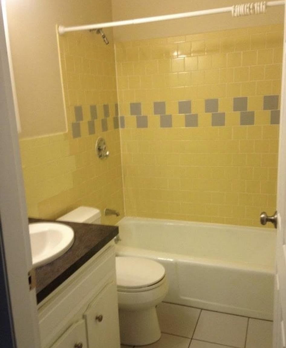 Yellow and gray tiled bathroom with toilet, sink, and bathtub.
