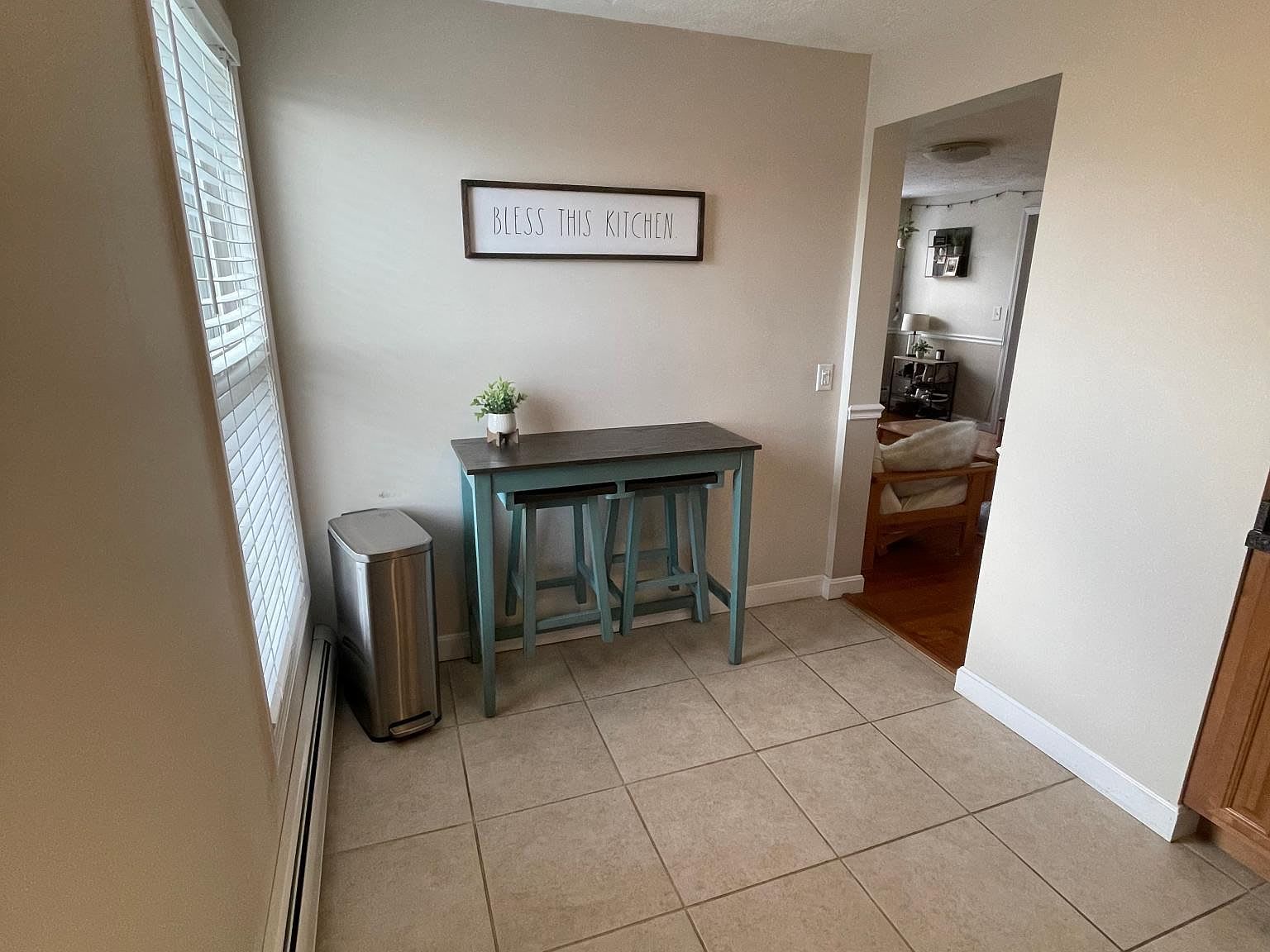 A small dining area with a table, stools, and a trash can, with a doorway leading to another room.