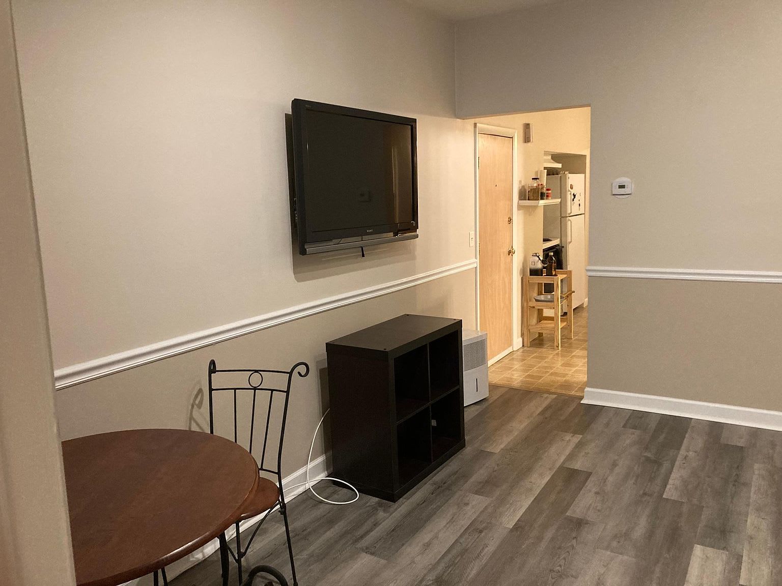 Room with a TV mounted on the wall, dark wood cabinet, small table, and doorway to another area.