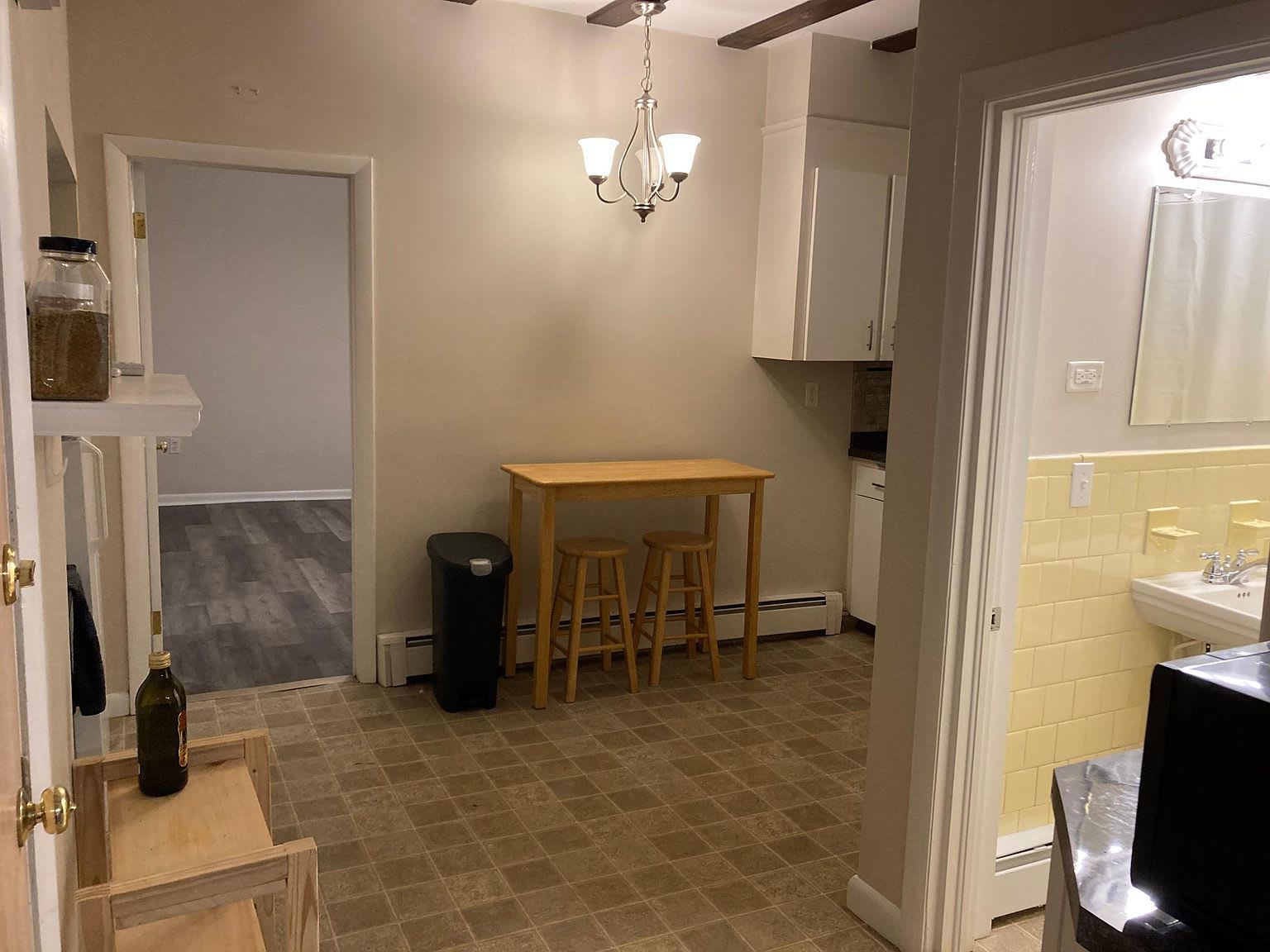 Small kitchen with table, stools, cabinets, and a doorway to another room.