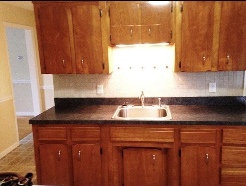 Kitchen with wooden cabinets, dark countertop, and a stainless steel sink.
