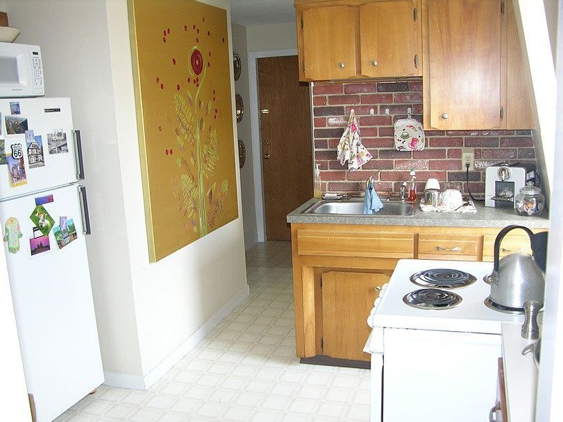 Small kitchen with white appliances, brick backsplash, and large yellow artwork.