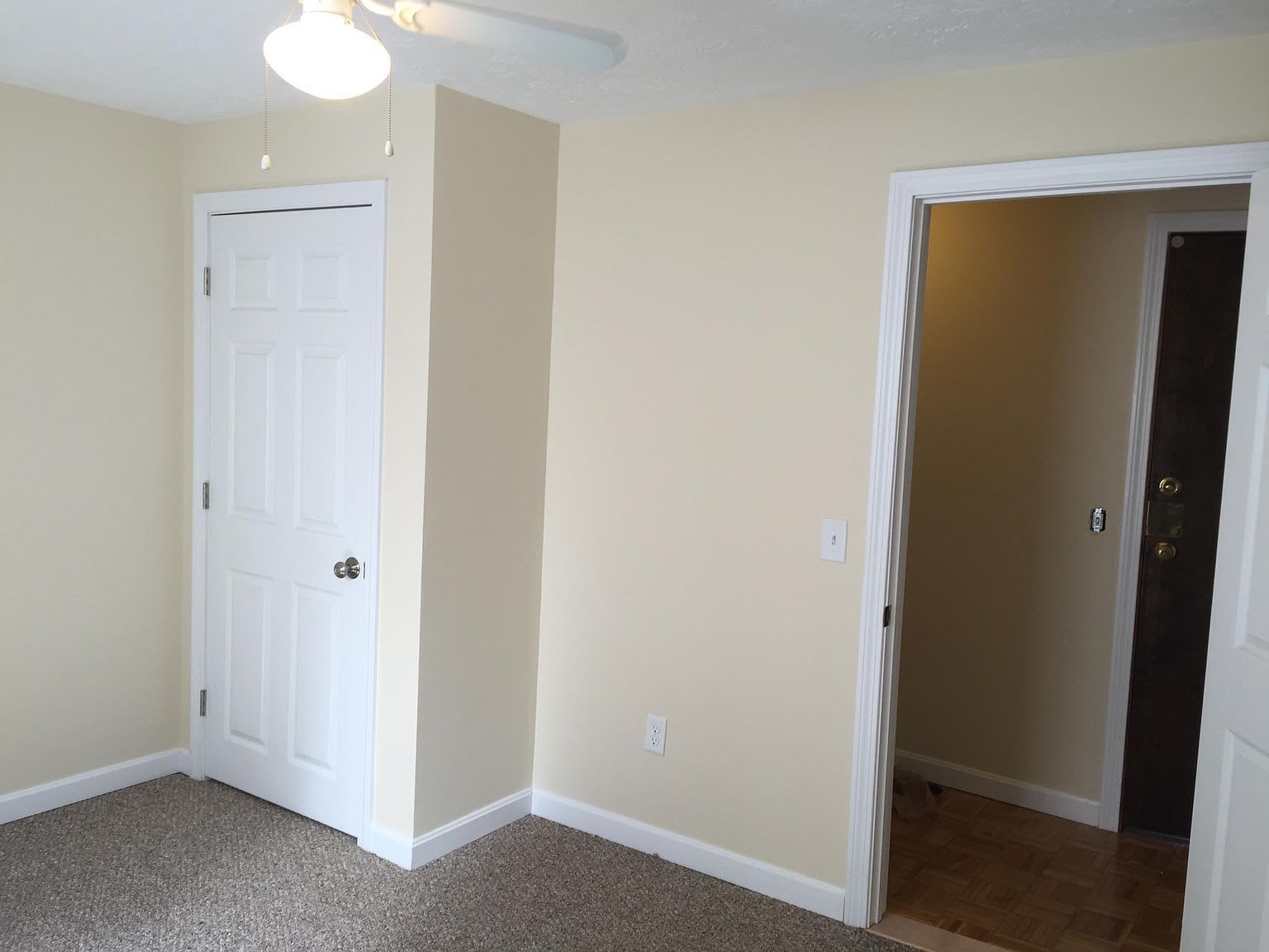 Empty room with beige walls, white door, and doorway to another room. Brown carpet.